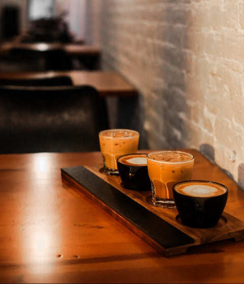 Hot and iced latte flight on a wooden table inside Arrowroot Coffee Lounge